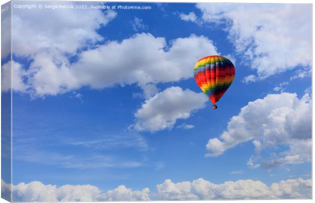 A motley multicolored hot air balloon raises a basket with tourists in the blue sky among white clouds. Canvas Print by Sergii Petruk