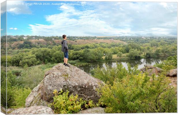 The teenager stands on top of a large stone boulder on the bank of the Southern Bug River and looks at the river below Canvas Print by Sergii Petruk
