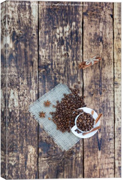 Grain coffee in a cup, which stands on a sackcloth from burlap. Cinnamon on a platter and tied with a rope. Anise stars complement the aroma of coffee. View from above. Canvas Print by Sergii Petruk