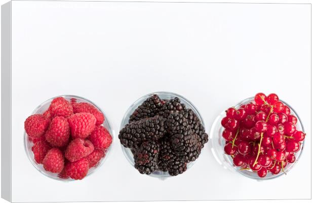 Raspberry, a big black blackberry and red currant are located in clear glass on a light background Canvas Print by Sergii Petruk