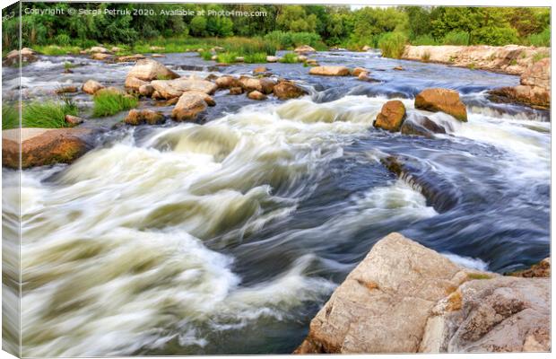 The rapid flow of the river in the blur, rocky shores, boulders and rapids, bright green vegetation on the other side of the shore. Canvas Print by Sergii Petruk