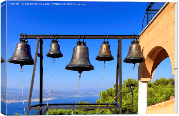 Closeup of bells against a blue sky, mediterranean pine and sea coast in blur, Greece, August 2019. Canvas Print by Sergii Petruk