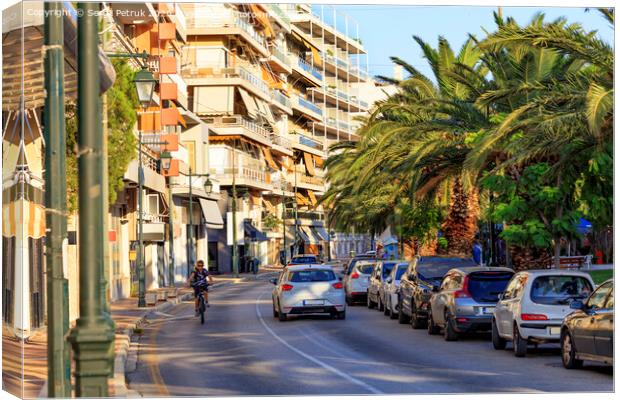 Street landscape of the summer city of Loutraki, Greece, with passing cars and a teenager on a bicycle. Canvas Print by Sergii Petruk