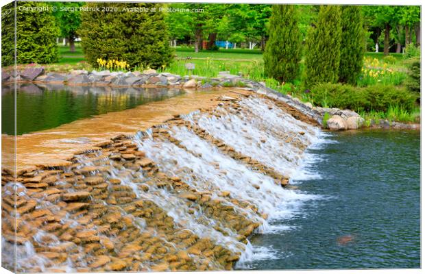 The waters of a beautiful decorative waterfall flow rapidly in a summer park. Canvas Print by Sergii Petruk