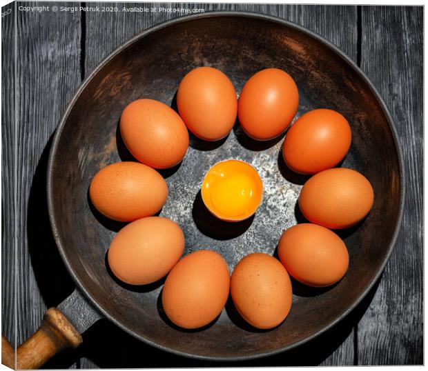 Brown chicken eggs in an old cast-iron frying pan look in the center at a broken egg with a bright yolk. Canvas Print by Sergii Petruk