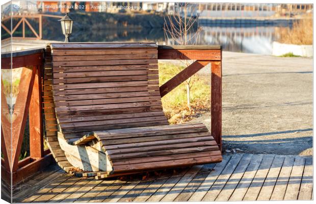 Outdoor furniture, a wooden chair on the river bank is illuminated by the rays of the bright sun against the background of the calm smooth surface of the water in blur. Canvas Print by Sergii Petruk