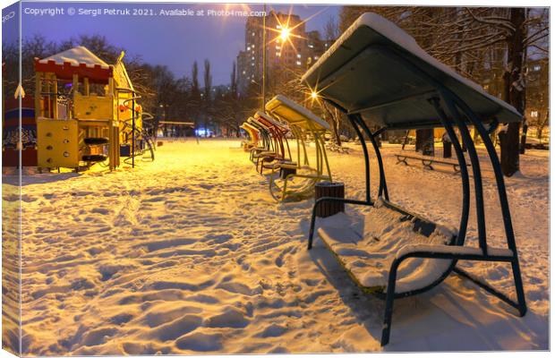 Wooden benches and a playground in the winter city evening park are covered with snow against the background of blue twilight. Canvas Print by Sergii Petruk