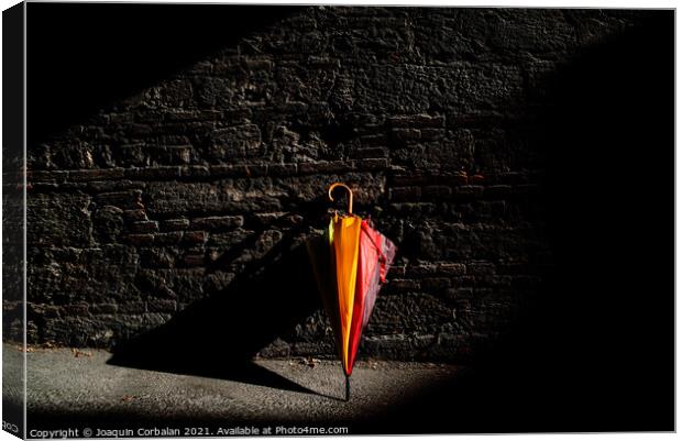 A beautiful colored umbrella rests folded against a brick wall i Canvas Print by Joaquin Corbalan