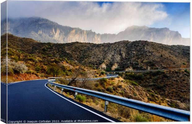 Winding road leads to high mountains with clouds to escape the r Canvas Print by Joaquin Corbalan