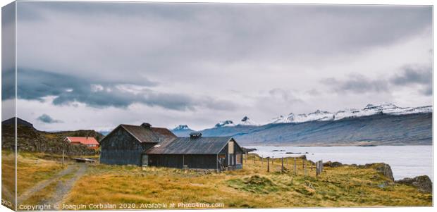 Village with farms in a rural area of the mountains of Iceland, with snowy mountains in the background. Canvas Print by Joaquin Corbalan