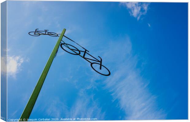 Post with the figure of some bicycles indicating the road, with blue sky and clouds in the background. Canvas Print by Joaquin Corbalan