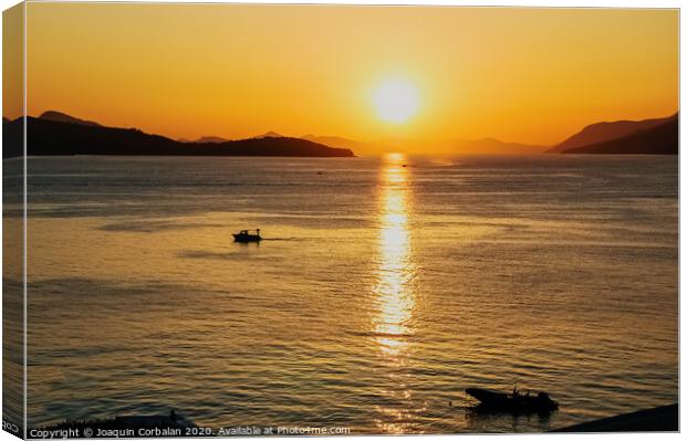 Sunset in a bay with mountains in the background and a small boat anchored. Canvas Print by Joaquin Corbalan