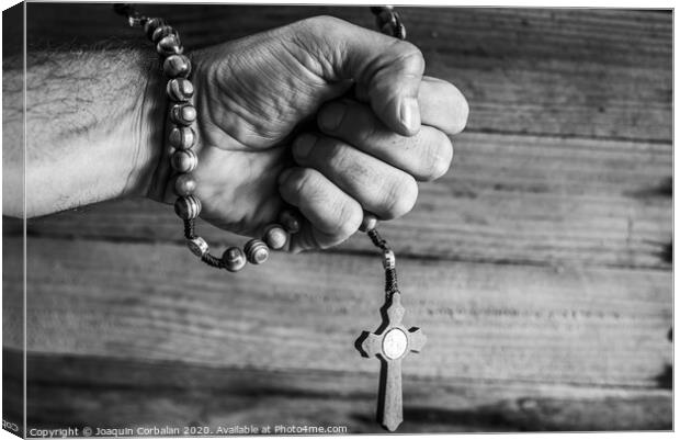 Hand of a religious person holds a Christian rosary during his prayers, unfocused background of woods in black and white. Canvas Print by Joaquin Corbalan