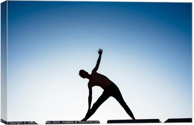 Silhouette of a man practicing yoga, isolated against the blue sky. Canvas Print by Joaquin Corbalan