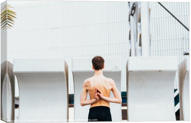 Young male athlete performing stretching exercises for back and arms in an urban place. Canvas Print by Joaquin Corbalan