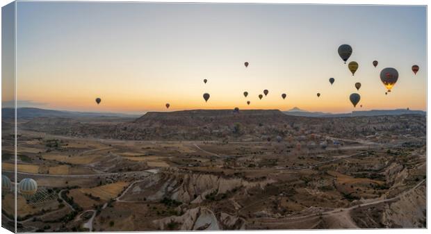 Cappadocia, Turkey - September 14, 2021: Wide angle Panorama aerial shot of colorful hot air balloons together floating in the sky at early morning in Goreme against volcanic hills Canvas Print by Arpan Bhatia
