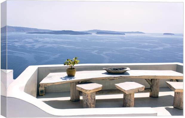 Santorini, Greece: A pot with flower or plant and a plate on a wooden table with wooden chair against beautiful sea ocean background with mountains Canvas Print by Arpan Bhatia
