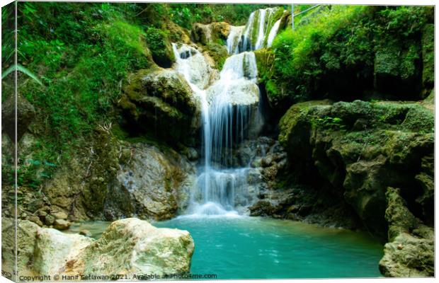 A waterfall flowing over rocks into a river. Canvas Print by Hanif Setiawan