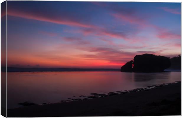 Silhouetted reflecting rock at sunset on sandbeach Canvas Print by Hanif Setiawan