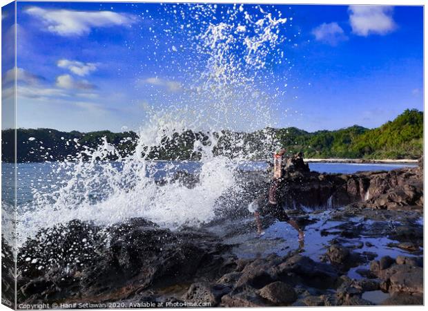 A big wave hits a man on a rock plateau Canvas Print by Hanif Setiawan