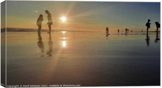 Silhouetted people in a row on a wet sand beach. Canvas Print by Hanif Setiawan