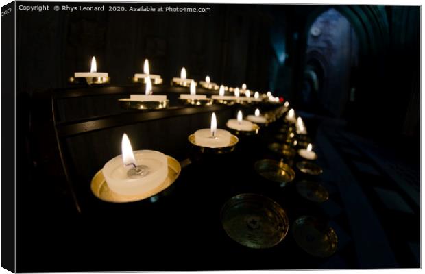 Prayer candles shine bright in a dark cathedral Canvas Print by Rhys Leonard