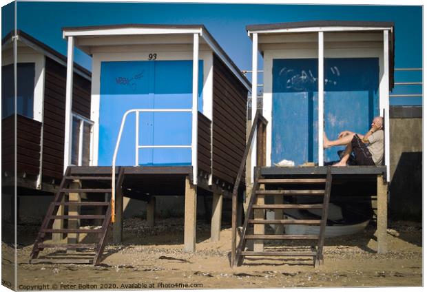 Beach huts at Thorpe Bay, Essex, with a person sitting on the floor talking on the phone. Canvas Print by Peter Bolton