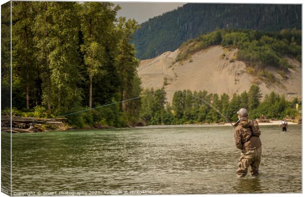 A fly fisherman hooked into a fish on a river with mountains and trees in the background Canvas Print by SnapT Photography