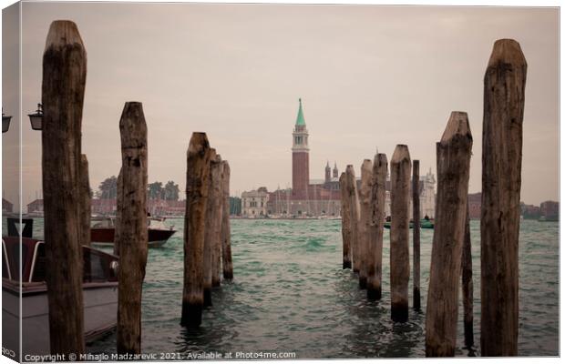 Wooden pillars at Venice bay symmetrically aligned pointing at Italian buildings in the back  Canvas Print by Mihajlo Madzarevic