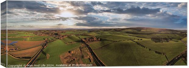 Panoramic aerial view of a scenic landscape with rolling hills, fields, and a winding road under a dramatic sky at sunset. Canvas Print by Man And Life