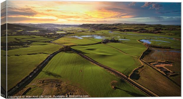 Aerial view of a lush green countryside at sunset with rolling hills, fields, and a winding river. Canvas Print by Man And Life
