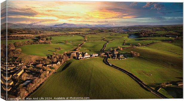 Aerial view of a scenic countryside at sunset with lush green fields, a small village, and a winding road leading towards distant hills. Canvas Print by Man And Life