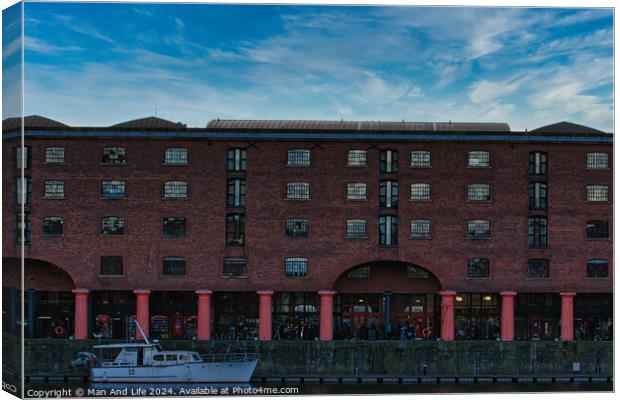 Brick warehouse with arched supports by a canal with a moored boat under a clear blue sky in Liverpool, UK. Canvas Print by Man And Life