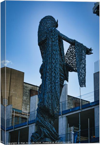 Artistic metal sculpture of a humanoid figure against a clear blue sky, with urban buildings in the background in Leeds, UK. Canvas Print by Man And Life