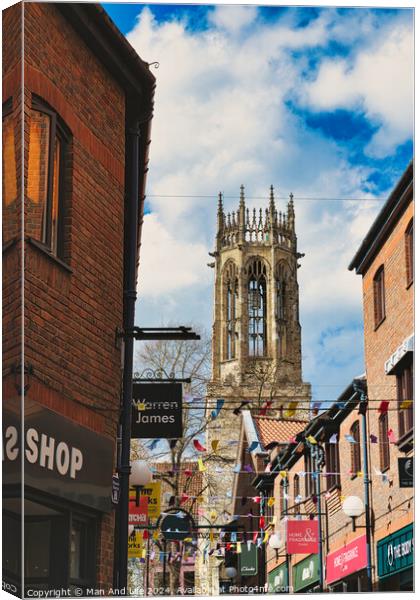 Quaint urban street with festive bunting leading to a historic church tower under a blue sky with fluffy clouds in York, North Yorkshire, England. Canvas Print by Man And Life