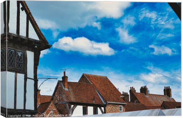 Quaint European village with traditional half-timbered houses and terracotta rooftops under a vibrant blue sky with fluffy clouds in York, North Yorkshire, England. Canvas Print by Man And Life