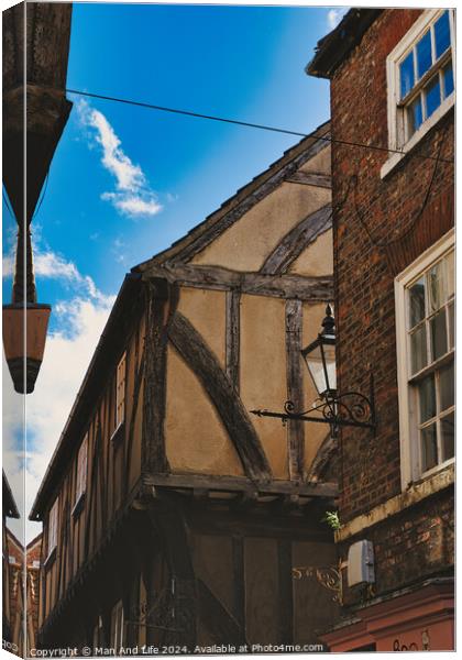 Quaint half-timbered building with exposed wooden beams under a clear blue sky, showcasing traditional architectural details and a vintage street lamp in York, North Yorkshire, England. Canvas Print by Man And Life