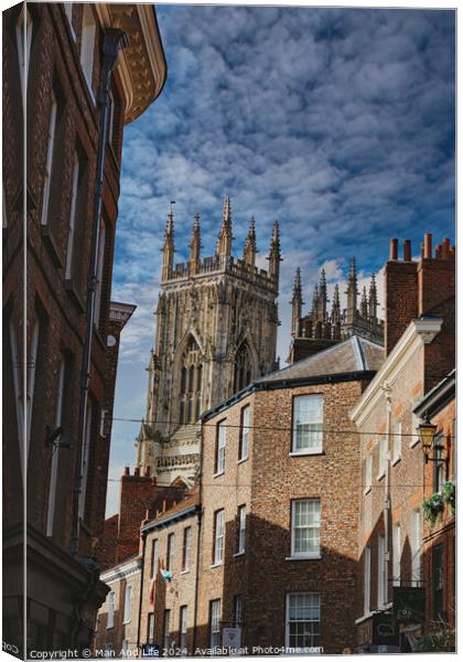 Quaint cobbled street leading to a majestic Gothic cathedral under a blue sky with wispy clouds, showcasing historical architecture and urban charm in York, North Yorkshire, England. Canvas Print by Man And Life
