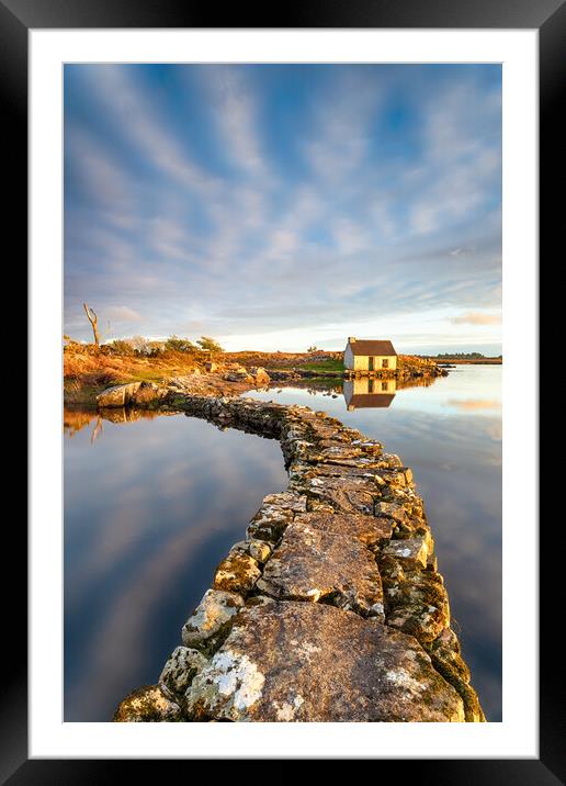 An old stone jetty across a lake leading to a small cottage Framed Mounted Print by Helen Hotson