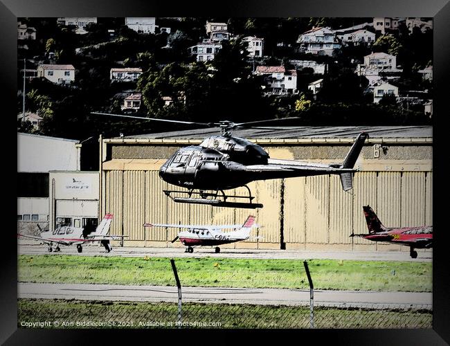 Helicopter hovering with planes in the background Framed Print by Ann Biddlecombe