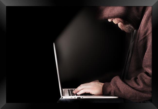 Hooded computer hacker using laptop Framed Print by Simon Bratt LRPS
