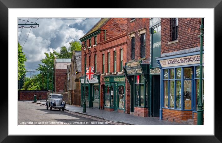 A vintage car in a Victorian village street Framed Mounted Print by George Robertson