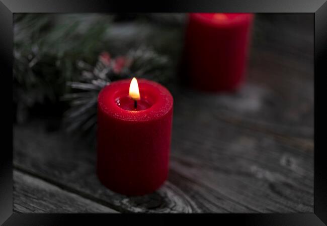 Close up of single red glowing candle with fir and wood dark bac Framed Print by Thomas Baker