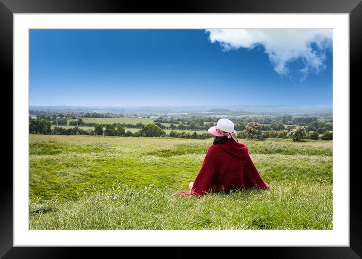 Woman sitting down in grassy farm fields while looking at the ho Framed Mounted Print by Thomas Baker