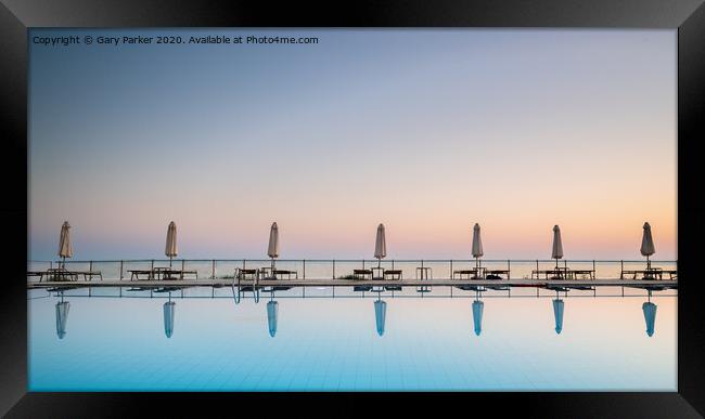 row of sunbeds and sun shades, reflecting in a still swimming pool, as the sun sets, in the Mediterranean	 Framed Print by Gary Parker
