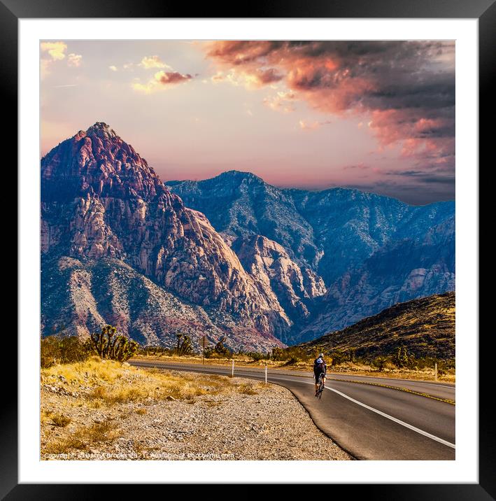 Rider Cycling on Road Through Desert Toward Mountains Framed Mounted Print by Darryl Brooks