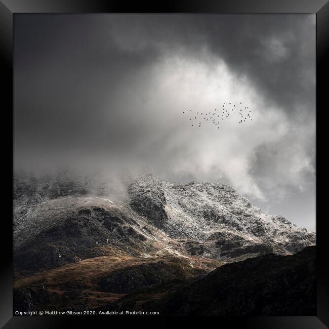 Stunning moody dramatic Winter landscape image of snowcapped Tryfan mountain in Snowdonia with stormy weather brooding overhead with birds flying high above Framed Print by Matthew Gibson