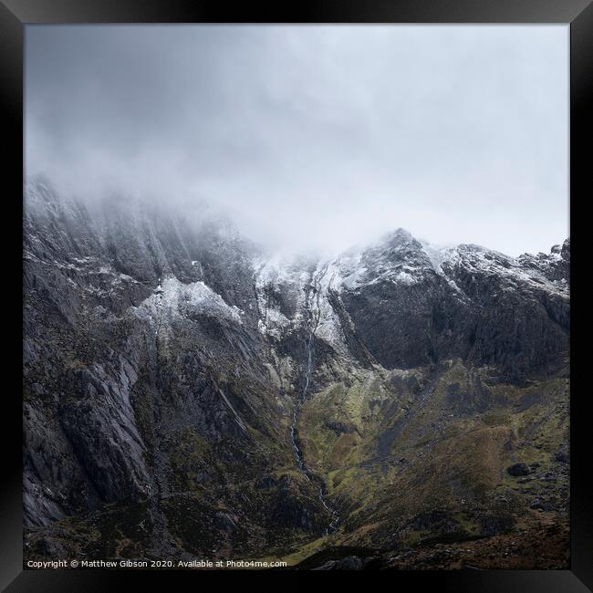 Stunning dramatic landscape image of snowcapped Glyders mountain range in Snowdonia during Winter with menacing low clouds hanging at the peaks Framed Print by Matthew Gibson