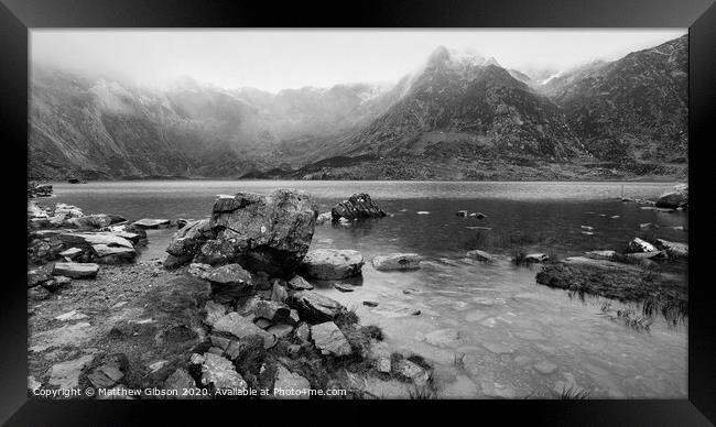 Beautiful moody Winter landscape image of Llyn Idwal and snowcapped Glyders Mountain Range in Snowdonia in black and white Framed Print by Matthew Gibson