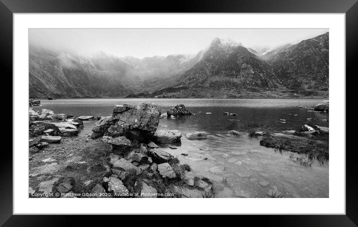 Beautiful moody Winter landscape image of Llyn Idwal and snowcapped Glyders Mountain Range in Snowdonia in black and white Framed Mounted Print by Matthew Gibson